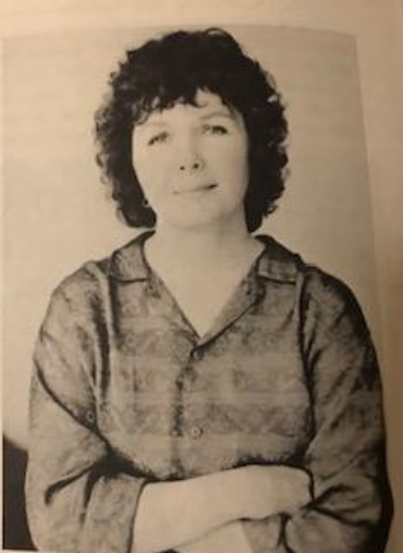 A black and white portrait of a woman with curly hair, wearing a patterned blouse, looking slightly to the side with a thoughtful expression.