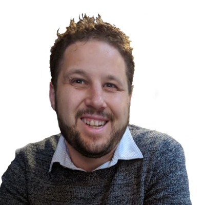 Smiling man with short curly hair and a beard, wearing a gray sweater over a collared shirt, set against a white background.