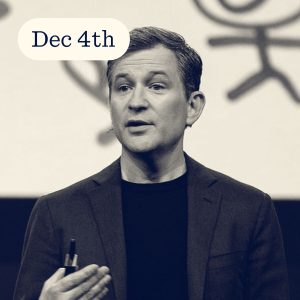 Speaker presenting on stage with a date overlay, holding a pen and gesturing, abstract background behind them.