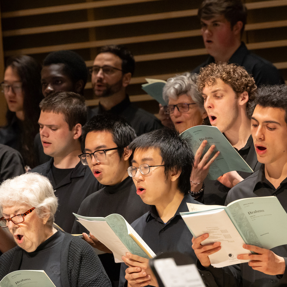 A diverse choir performing with music sheets, showcasing expressions of focus and emotion during a music piece.