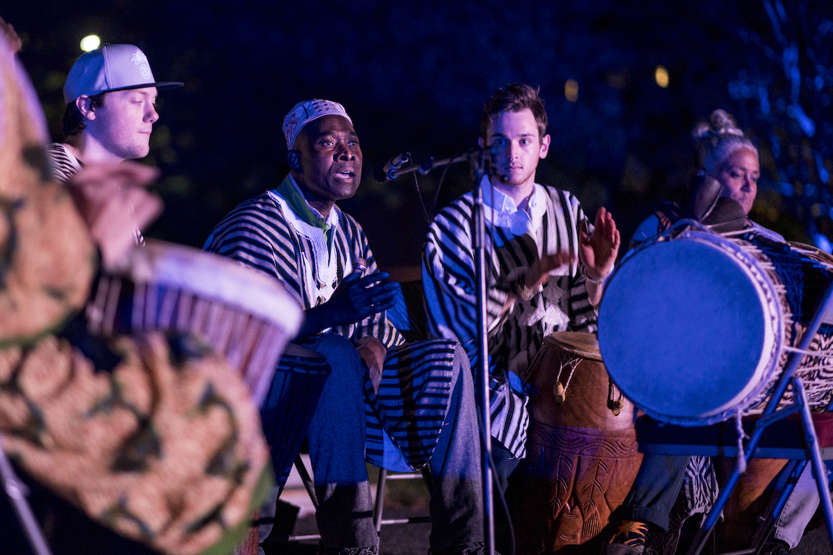 Musicians performing with drums at night, wearing matching striped outfits, under dramatic blue lighting.
