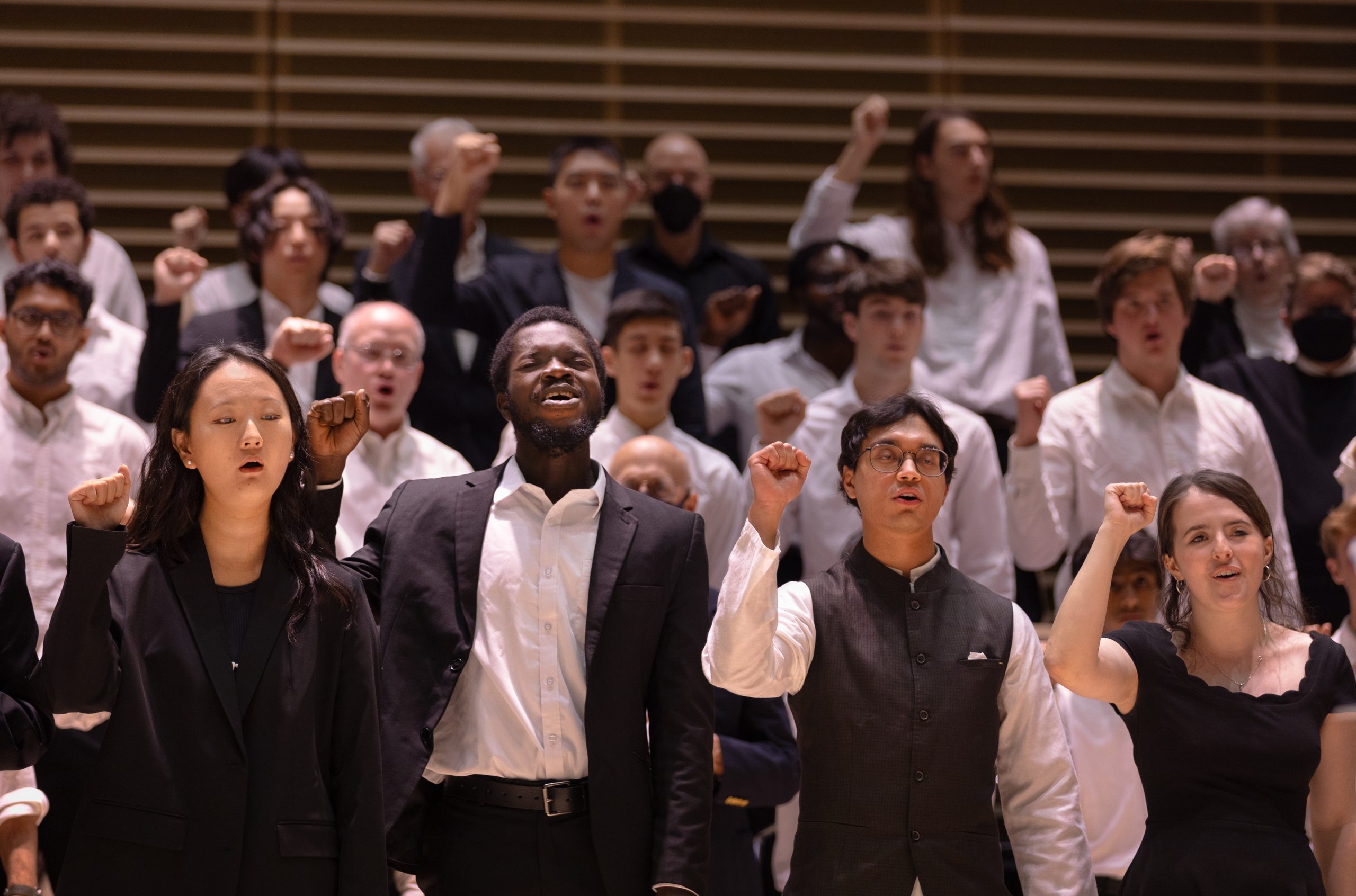 Diverse choir performing with raised fists, dressed in formal attire, conveying a message of unity and empowerment.