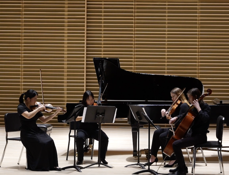 Classical musicians performing on stage with a grand piano and sheet music in a modern concert hall setting.