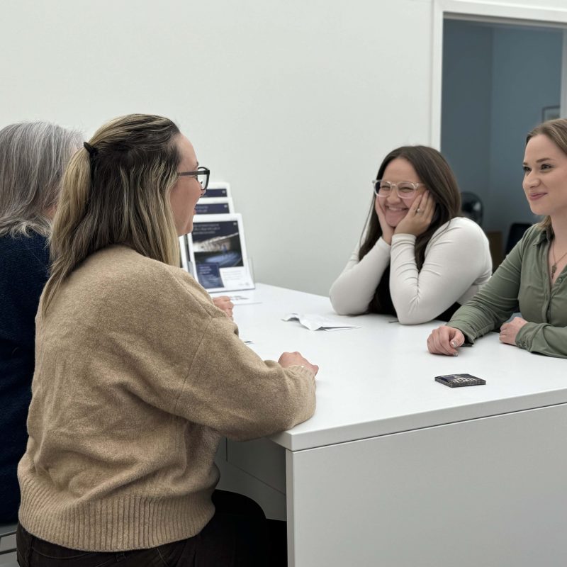 Four individuals engaged in a conversation around a white table, with pamphlets and documents in front of them.