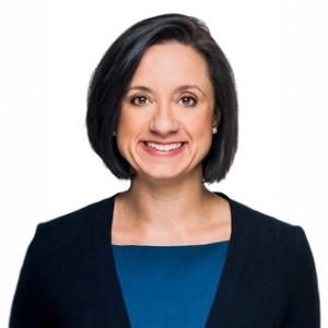 Professional headshot of a woman with shoulder-length black hair, wearing a black blazer over a blue top, smiling at the camera.