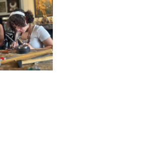 Person focused on a crafting project, using tools, surrounded by artistic items in a creative workspace.