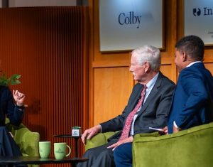 An engaging discussion between three speakers on a stage with green chairs and a backdrop featuring news logos.
